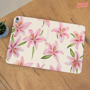 May include: A cream-colored tablet case featuring a repeating pattern of pink lilies with green leaves. The lilies have yellow stamens and are scattered across the surface. The text "Whimsical Something Co" is in the upper right corner.