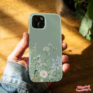 May include: A light green phone case with a floral design featuring white flowers and green stems. The case has a camera cutout and a clear back.