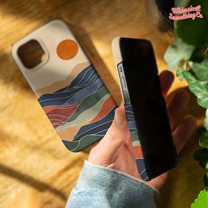 May include: A phone case with a minimalist design featuring a sunset over a landscape of colourful mountains. The case is beige with a subtle texture.