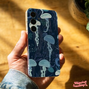 May include: A clear phone case with a dark blue background and a pattern of white jellyfish. The case has a cutout for a triple camera lens.