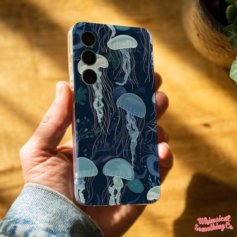 May include: A clear phone case with a dark blue background and a pattern of white jellyfish. The case has a cutout for a triple camera lens.