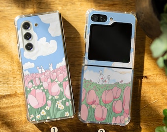 May include: Two clear phone cases with a whimsical design featuring pink tulips, green grass, and white bunnies against a blue sky. The case on the left is for a standard phone, while the case on the right is for a flip phone.
