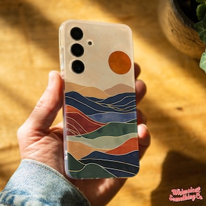 May include: A clear phone case with a colorful abstract landscape design. The design features a sunset with a large orange sun, blue and green mountains, and gold lines.