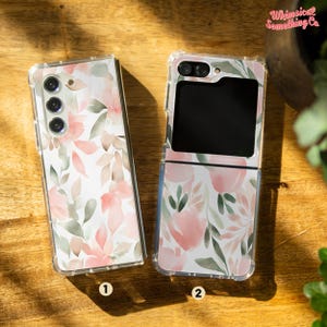 Pode incluir: Duas capas transparentes para telefone com um design floral. As capas são para um telefone Samsung Galaxy Z Flip. O design apresenta flores cor-de-rosa e verdes em aquarela sobre um fundo branco.