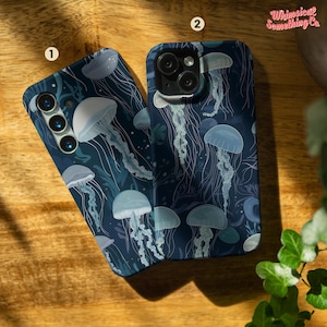Op de afbeelding: Twee telefoonhoesjes met een donkerblauwe achtergrond en een patroon van kwallen in blauw- en wittinten. De hoesjes liggen op een houten oppervlak. De tekst "Whimsical Something Co" is zichtbaar.