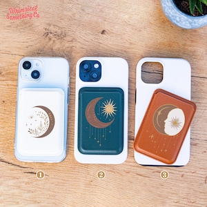 May include: Three white phone cases with attached phone grips featuring celestial designs. The grips display a crescent moon, sun, and stars in brown, gold, and white. The phone cases are on a wooden surface. The top left corner of the image has the text "Whimsical Something Co."
