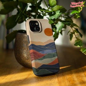 Puede incluir: Una funda para tel&eacute;fono con un dise&ntilde;o minimalista que presenta una puesta de sol sobre una cordillera en tonos azules, verdes, rojos y naranjas. La funda tiene un borde negro.
