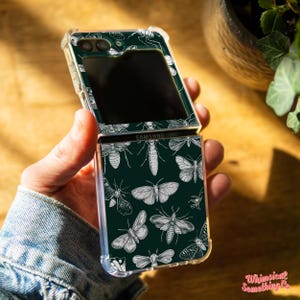 May include: A clear phone case with a green background and white butterfly illustrations. The case is designed for a Samsung Galaxy Z Flip phone.