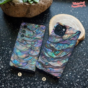 May include: Two rectangular phone cases featuring an iridescent, multi-coloured abalone shell pattern with wavy, overlapping textures in shades of blue, purple, green, and silver. Each case has a camera cutout and the number 1 or 2 printed below.