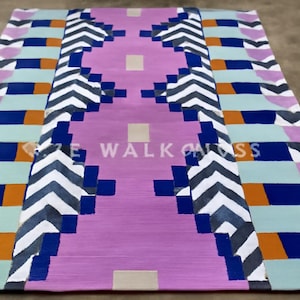 May include: A rectangular rug with a geometric design. The rug features a central lavender-colored section flanked by patterns in blue, white, orange, and light green. The text "SIZE WALK ON SS" is visible on the rug.