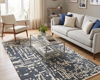 May include: A contemporary living room scene with a dark blue and cream geometric patterned rug. The room includes a light grey sofa with blue and cream cushions, a glass coffee table, and a wooden armchair. Artwork and a mirror are on the walls.