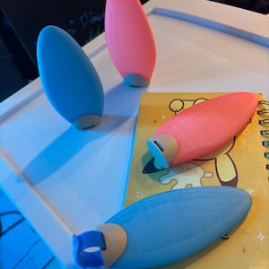Könnte beinhalten: Drei kleine, farbige, eiförmige Objekte. Zwei sind blau und eines ist rosa. Die Objekte bestehen aus einem glatten, gummiartigen Material.