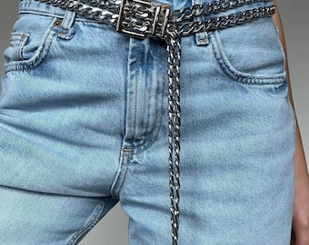 May include: A silver chain belt with a double layer design. The belt has a silver clasp and a long chain that hangs down to the wearer's thigh.