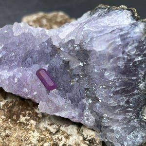 May include: A small, deep purple amethyst geode with a single, bright red ruby crystal embedded in the centre.