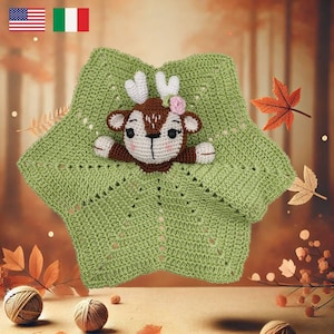 May include: A green crocheted baby blanket with a brown and white crocheted deer toy inside. The blanket has a square shape with a scalloped edge. The deer toy has a pink flower on its head.