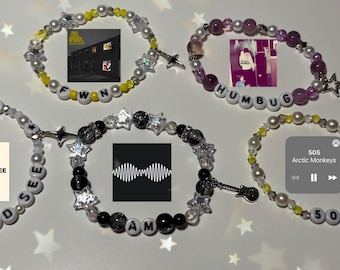 May include: Five beaded bracelets with white, black, yellow, and purple beads. Each bracelet features a different design, including star and guitar charms, and album art. The bracelets spell out "SUCK IT AND SEE", "AM", "HUMBUG", "FWN", and "505".