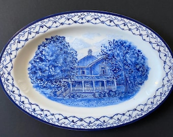 May include: Oval serving platter with a blue and white design. The center features a blue illustration of a house with trees. The rim has a blue floral pattern on a white background.