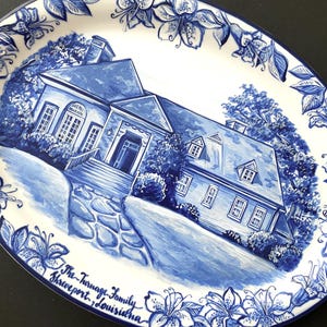 May include: A blue and white hand-painted ceramic oval platter featuring a house with a blue roof and white trim. The house is surrounded by trees and flowers. The text "The Turnage Family Shreveport, Louisiana" is written in blue cursive at the bottom of the platter.