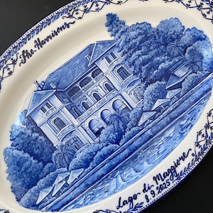 Puede incluir: Plato ovalado de cerámica con un diseño azul y blanco pintado a mano. El plato presenta una ilustración detallada de una villa junto al lago con árboles y agua. Las palabras "The Harrisons" y "Lago di Maggiore 8.9.2025" están escritas en el plato.
