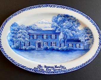 May include: A blue and white hand-painted ceramic oval platter with a depiction of a house, trees, and clouds. The text "The Hageney Family 1030 Tenby Road Berwyn PA" is written on the bottom of the platter.