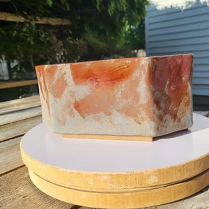 May include: A rectangular ceramic planter with a geometric design. The planter features a blend of orange, red, and white hues. The planter is sitting on a white surface.