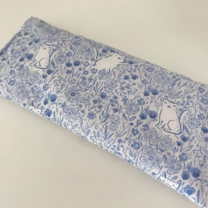 Puede incluir: Una almohada para los ojos azul y blanca con un patr&oacute;n floral y gatos blancos. La almohada es rectangular y tiene una costura en el medio.