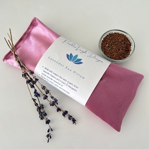 May include: A pink satin eye pillow filled with flax seeds and lavender flowers. The pillow is labeled "Lavender Eye Pillow" and "Kendra Leigh Designs".