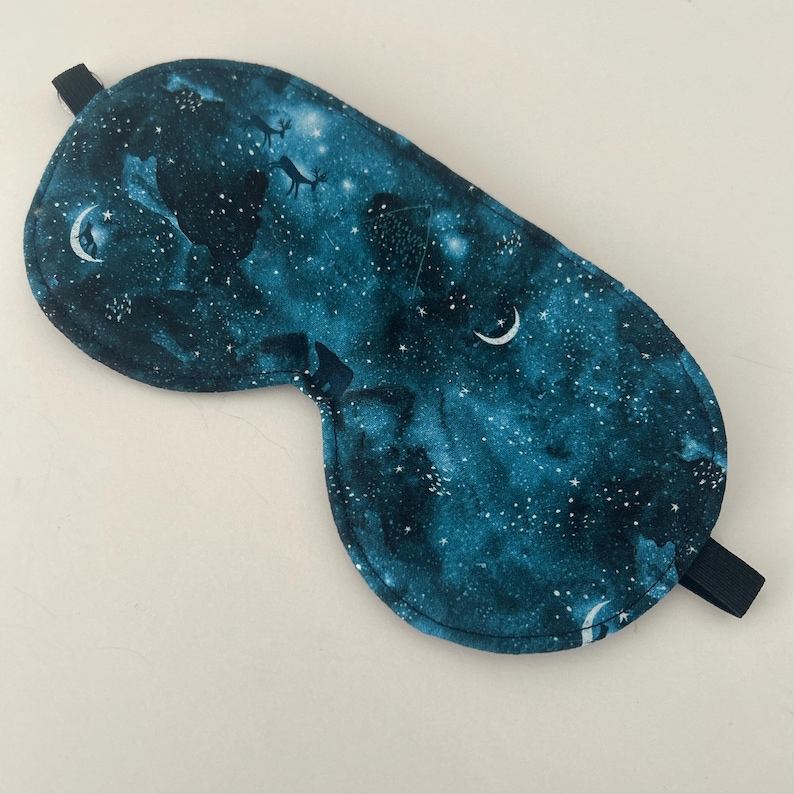 May include: A dark blue sleep mask with a galaxy print featuring white stars and crescent moons. The mask has an elastic strap.