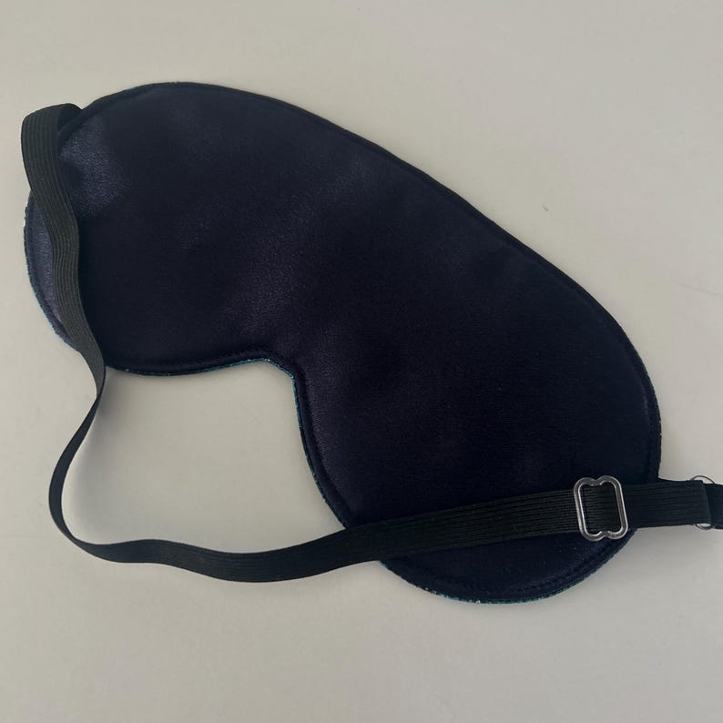May include: A black sleep mask with an adjustable elastic strap. The mask is made of a soft, comfortable material and is designed to block out light.
