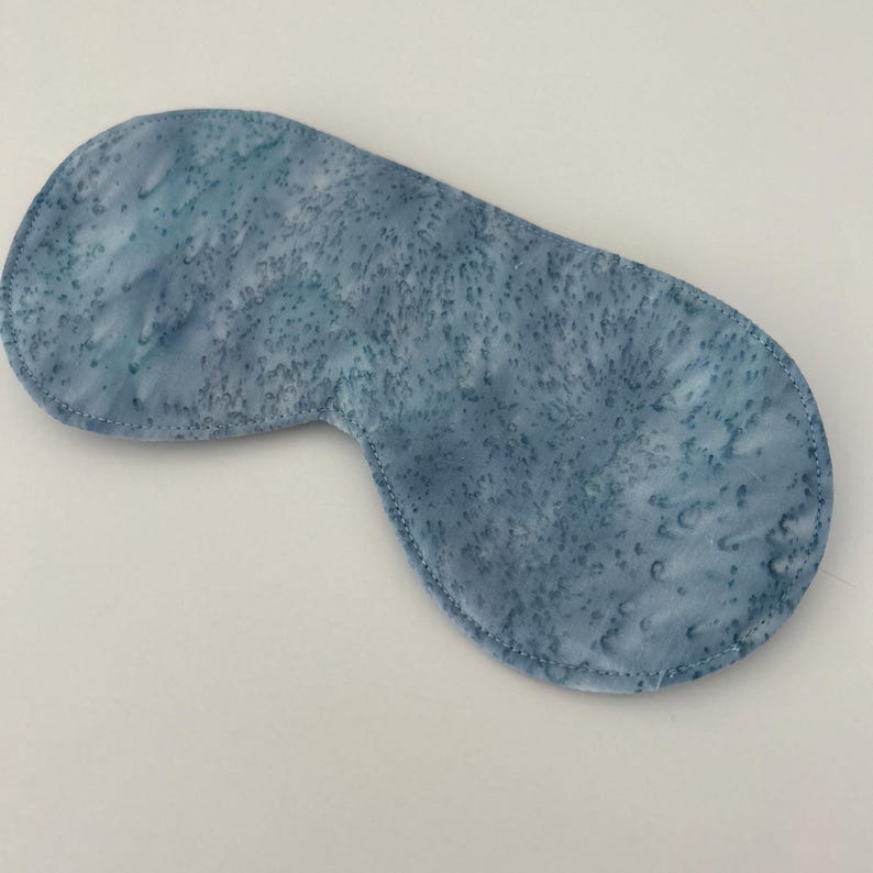Puede incluir: Una m&aacute;scara para dormir azul con un patr&oacute;n de tie-dye blanco y azul. La m&aacute;scara est&aacute; hecha de tela suave y est&aacute; dise&ntilde;ada para bloquear la luz.