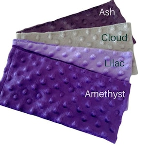 Puede incluir: Cuatro muestras de tela en tonos de morado, gris y lila. Las muestras est&aacute;n etiquetadas como "Amatista", "Lila", "Nube" y "Ceniza".