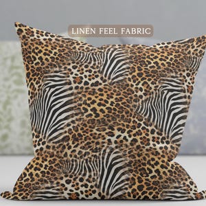 May include: A square throw pillow featuring a repeating pattern of black and white zebra stripes layered over a brown and black leopard print. The text LINEN FEEL FABRIC is printed in a small rectangular box at the top center of the pillow.