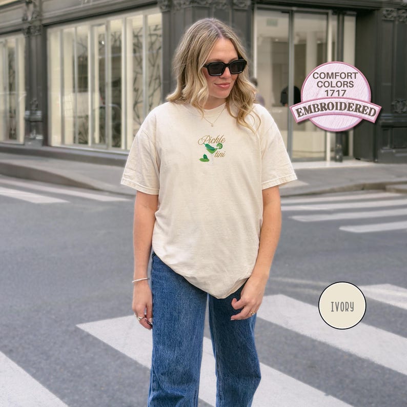 May include: Ivory-colored t-shirt with embroidered "Pickle Time" design in green. The shirt is a Comfort Colors 1717 style. The model is wearing blue jeans and sunglasses.