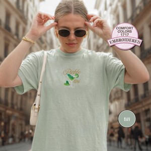 May include: A light green t-shirt with the embroidered text "Pickle Martini" and a matching graphic of a martini glass. The shirt has short sleeves and a crew neck. The shirt is labeled "Comfort Colors 1717 Embroidered".