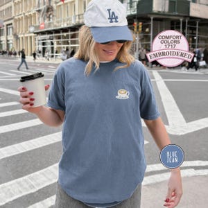 Puede incluir: Camiseta azul vaquera de manga corta con un dise&ntilde;o de taza de caf&eacute; bordada. La camiseta es de estilo Comfort Colors 1717. Se lleva una gorra de b&eacute;isbol blanca y azul.