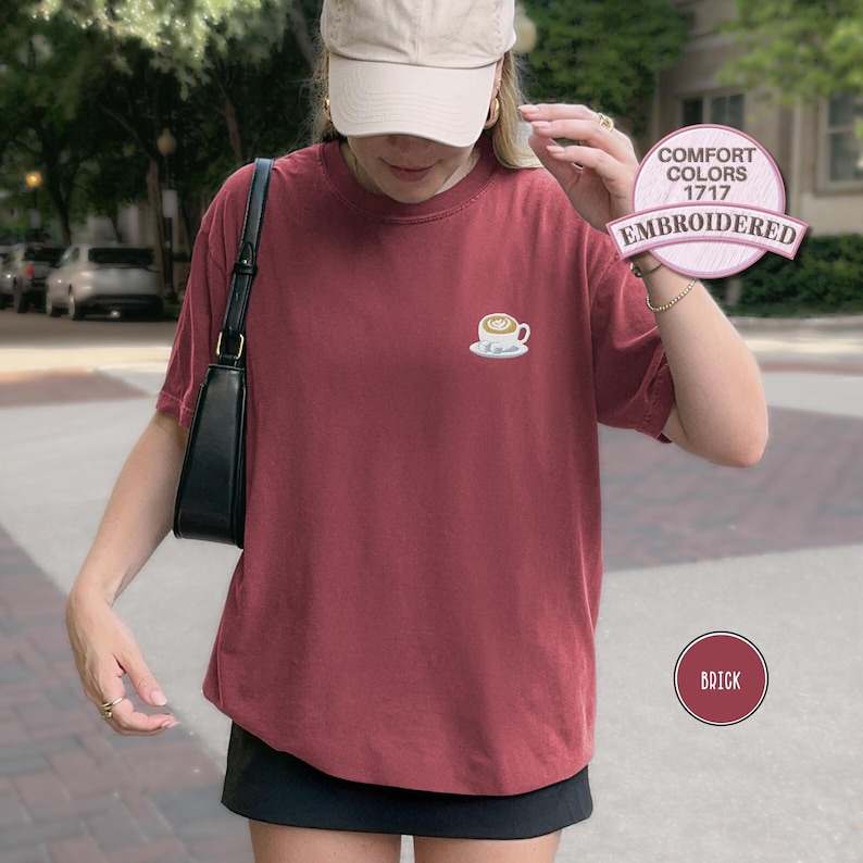 Puede incluir: Camiseta color ladrillo con un peque&ntilde;o dise&ntilde;o de taza de caf&eacute; bordada en el pecho. La camiseta es de estilo Comfort Colors 1717. La imagen tambi&eacute;n incluye un bolso negro y una gorra beige.