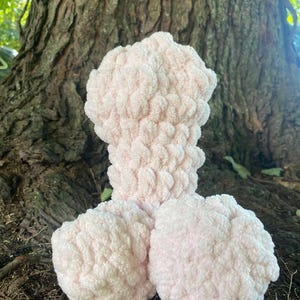 May include: A pink crocheted plush toy shaped like a human body. The toy is made of soft, fluffy yarn and has a textured surface.