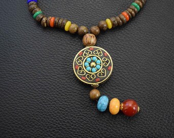 Könnte beinhalten: Eine Holzperlenkette mit einem runden Anhänger mit einem blauen und goldenen Design. Der Anhänger ist von einem roten Rand umgeben. Die Kette hat eine Vielzahl von bunten Perlen, darunter braun, rot, gelb und grün.