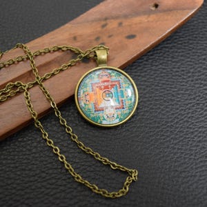 May include: A gold chain necklace with a round pendant featuring a colourful mandala design. The pendant is made of glass and has a metal frame.