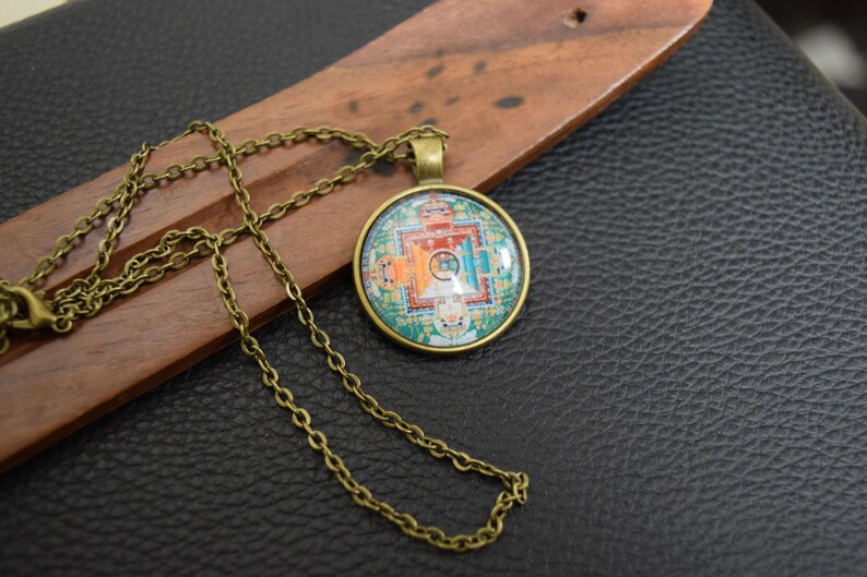 May include: A gold chain necklace with a round pendant featuring a colourful mandala design. The pendant is made of glass and has a metal frame.