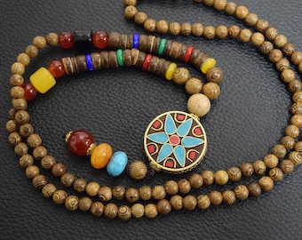 Könnte beinhalten: Eine braune Holzperlenkette mit einem bunten Blumenanhänger. Der Anhänger hat eine blaue Mitte mit roten und goldenen Akzenten.