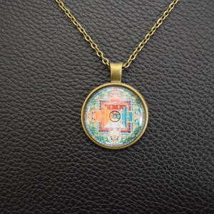May include: A gold chain necklace with a round pendant featuring a colourful mandala design. The pendant is made of glass and has a bronze-coloured metal frame.
