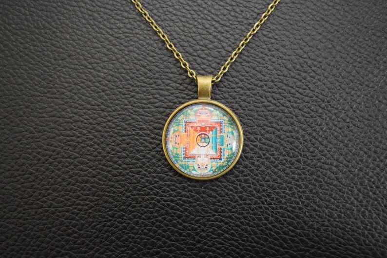 May include: A gold chain necklace with a round pendant featuring a colourful mandala design. The pendant is made of glass and has a bronze-coloured metal frame.