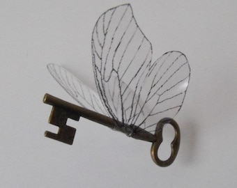 May include: A key with a delicate butterfly design made of translucent fabric with black stitching. The key is made of metal and has a traditional design.