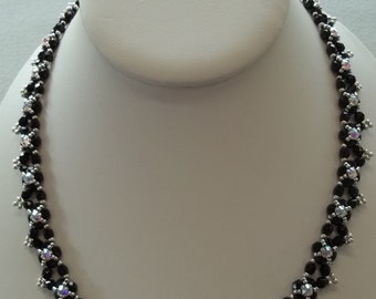 May include: A black and silver beaded necklace with a delicate, intricate design. The necklace is made with small, round beads and features a repeating pattern of small silver beads interspersed with larger black beads.
