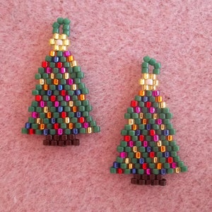 Könnte beinhalten: Ein Paar Ohrringe in Form von Weihnachtsbäumen. Die Bäume sind grün mit roten, orangen, gelben, blauen und goldenen Perlen. Die Spitzen der Bäume sind golden und die Böden sind braun.