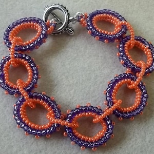 May include: A purple and orange beaded bracelet with a silver clasp. The bracelet is made of small, round beads that are strung together in a pattern of alternating colors.