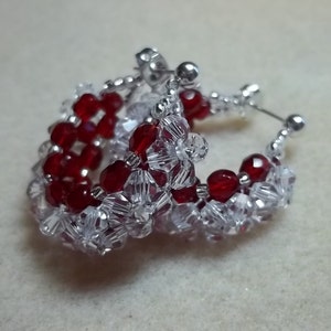 Puede incluir: Un par de pendientes de aro de plata con cuentas de cristal rojo y transparente. Los pendientes están hechos con pequeñas cuentas facetadas que crean un efecto brillante.