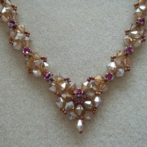 May include: A delicate gold and pink crystal necklace with a heart-shaped design. The necklace is made with small, faceted crystals and features a central heart-shaped cluster of crystals.