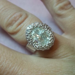 May include: A silver ring with a clear oval-shaped gemstone surrounded by small silver beads.